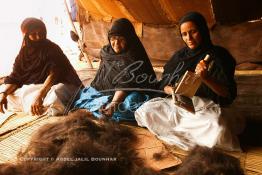 Image du Maroc Professionnelle de  Des femmes du désert préparent le fil de laine de chameau sous une tente durant le grand Moussem, Samedi 18 septembre 2004, aux environ de Tan Tan dans un site désertique sur lequel la ville, a toujours accueilli la majorité des tribus et des grandes familles nomades du désert lors d'un grand Moussem, danses chants, course de chameaux et fantasia font partie des festivités. (Photo / Abdeljalil Bounhar) 